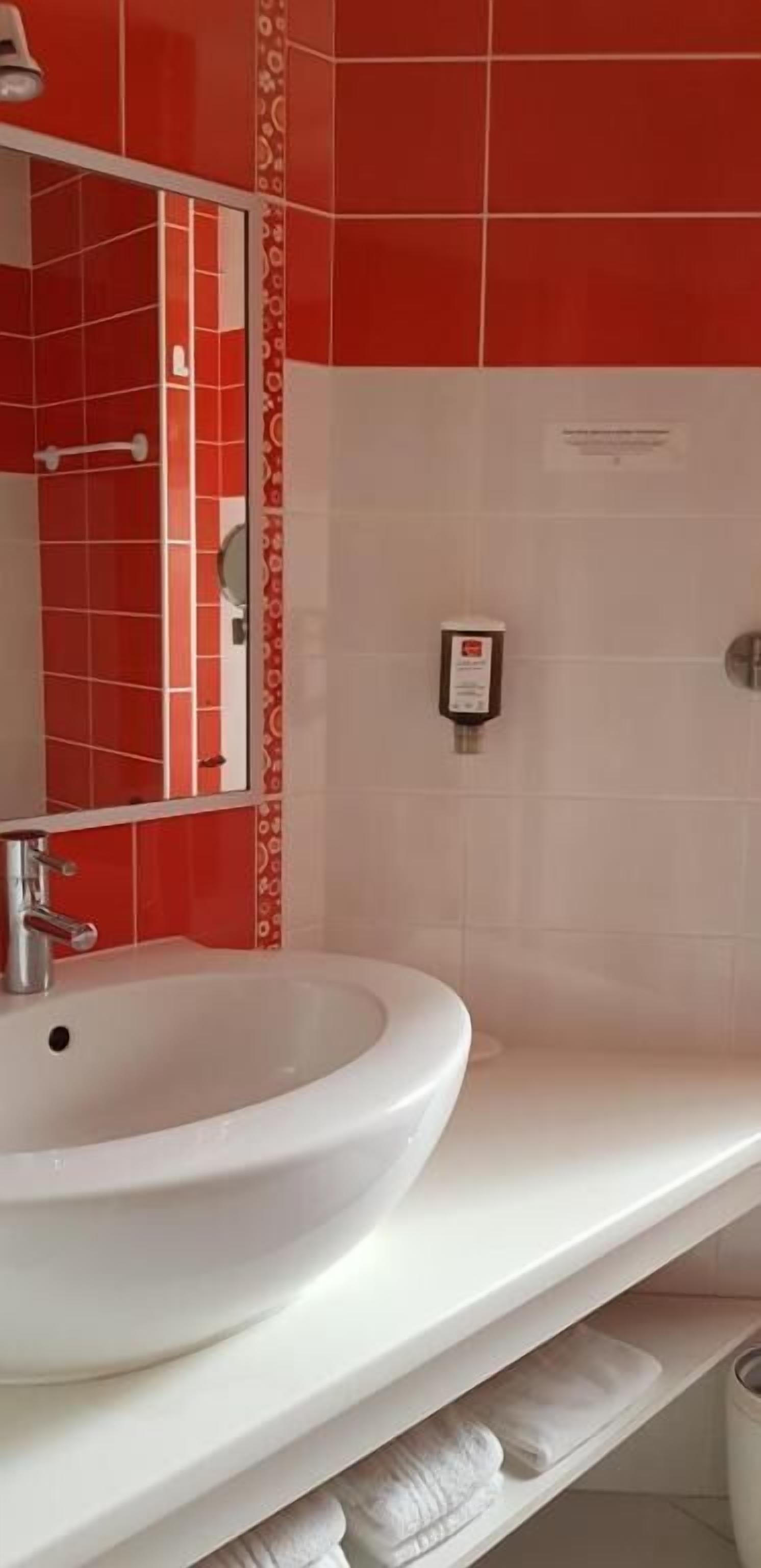 A bathroom with a white sink, a mirror, and red and white tiled walls.