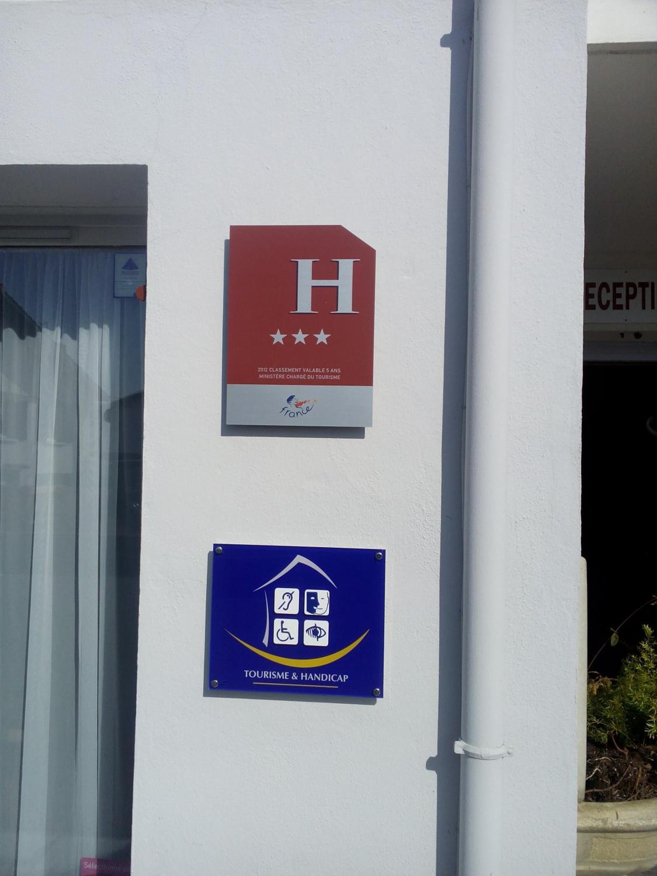 Un edificio con un cartel que indica que es un hotel de 5 estrellas, un letrero de servicios turísticos y para personas con discapacidad, y un área de recepción parcialmente visible.