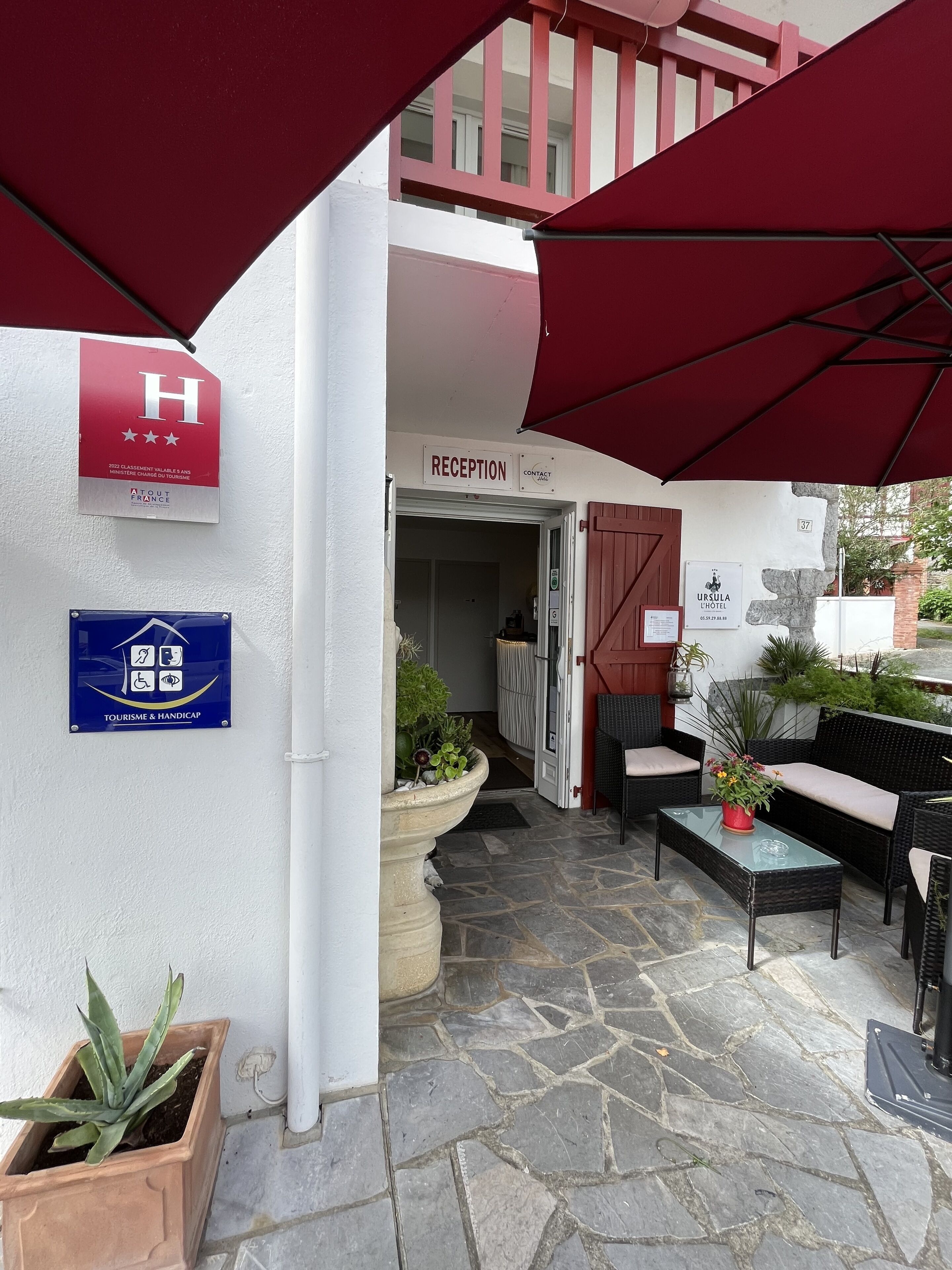 A hotel reception area with a sign indicating it is a 2020-classified hotel. There is a reception desk, a sign for the hotel named "Ursula L Hotel," and a sign for "Tourisme & Handicap."