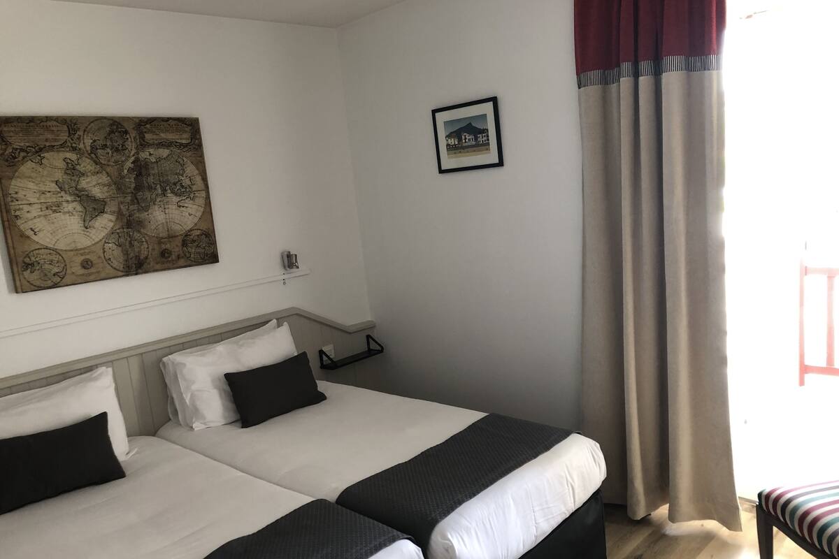 Een hotelkamer met twee bedden, een wereldkaart aan de muur, een ingelijst schilderij en een raam met gordijnen.