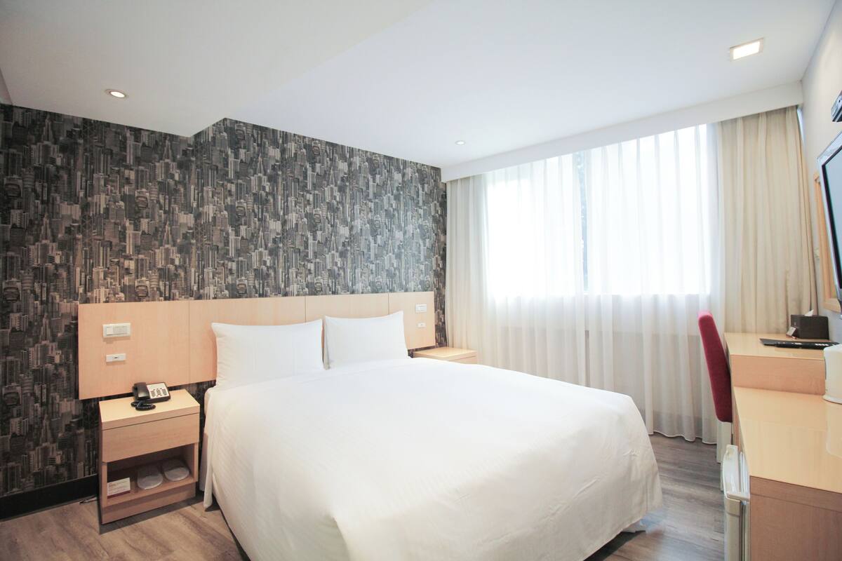 Una habitación de hotel con una cama grande, un escritorio con silla, una mesita de noche y un teléfono.
