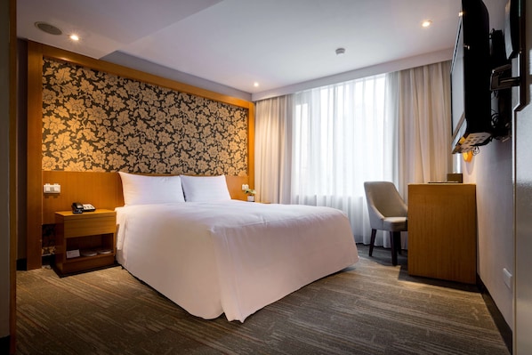 A hotel room with a large bed, a desk, a chair, and a television.