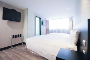 A hotel room with a bed, a TV mounted on the wall, a window with blinds, and a wooden floor. - Hotel B (Taipei)
