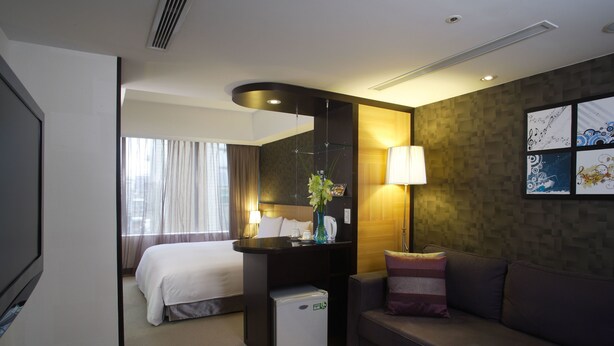 A hotel room with a bed, a small desk with a lamp, a sofa, and a wall with artwork. - Hotel B (Taipei)