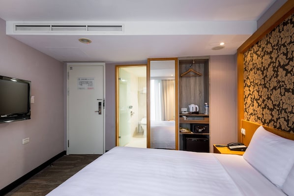 A hotel room with a bed, a television, a wardrobe, a mirror, a bedside table with a phone, and a bathroom visible through an open door. - Hotel B (Taipei)
