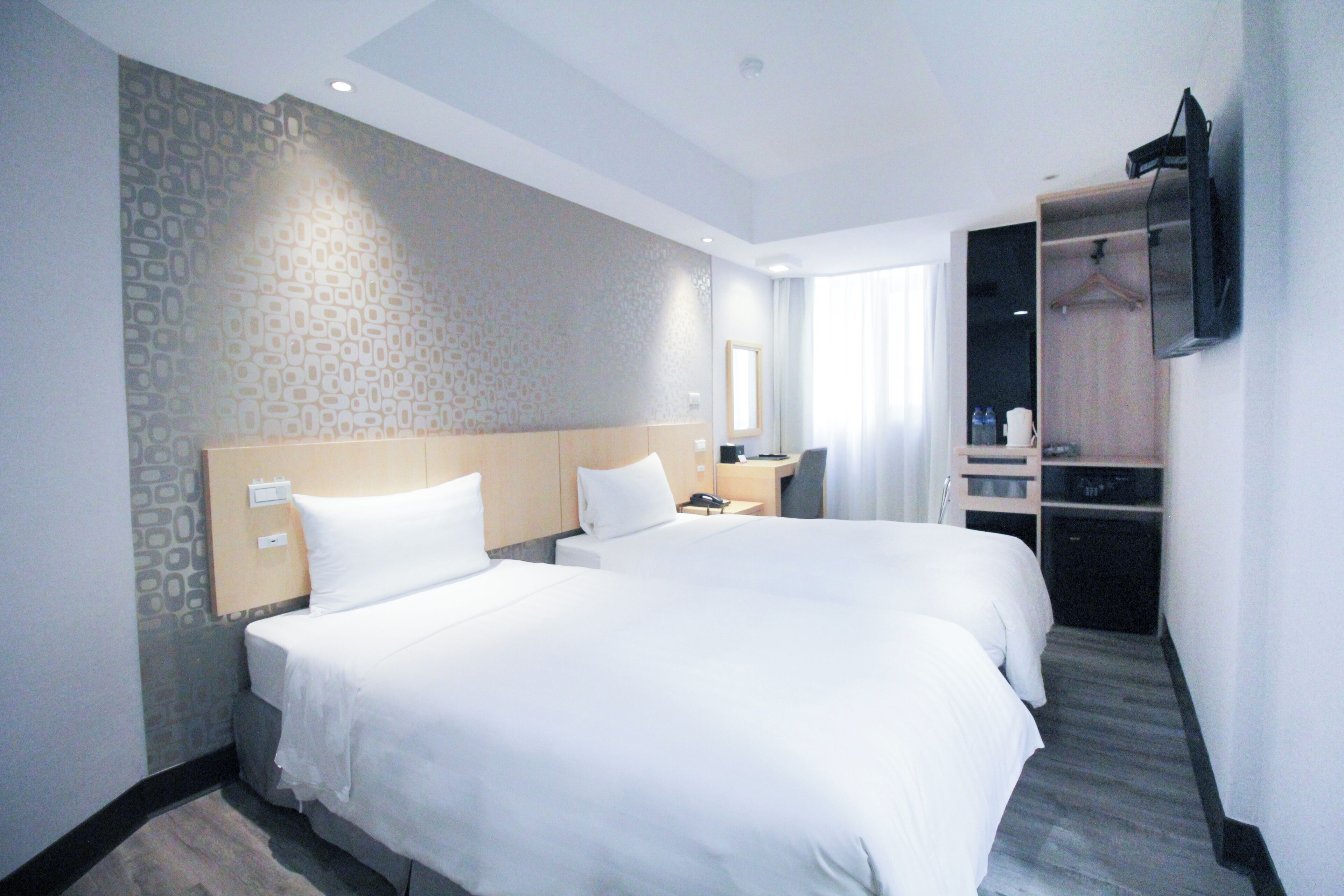 A hotel room with two beds, a desk, a wardrobe, and a TV mounted on the wall.