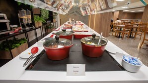 Un bufé con diferentes opciones de comida, incluyendo ollas rojas con la etiqueta 'Salsicha' y 'Sausage'.