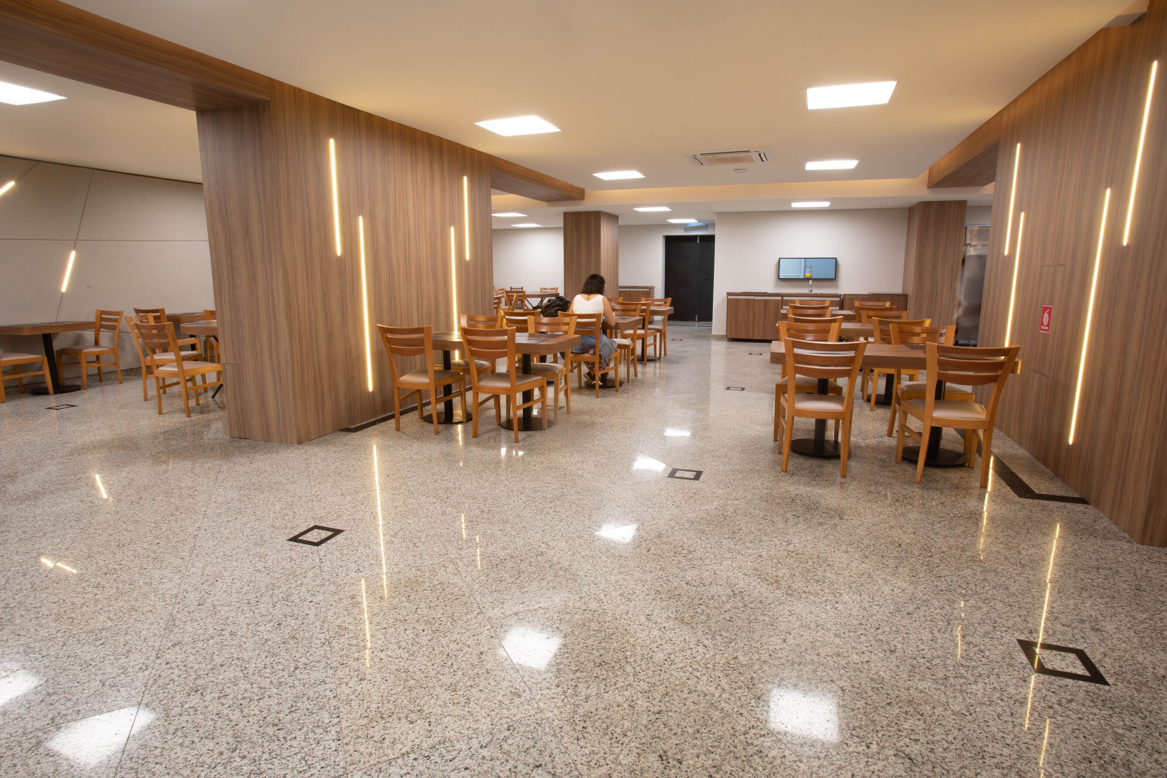 Una amplia sala de conferencias con múltiples mesas y sillas, paneles de madera y un suelo pulido.