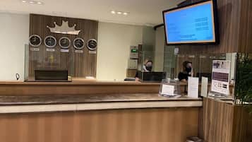 A reception desk with a digital screen, wooden paneling, and a clock.