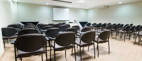 A conference room with rows of chairs, a projector screen, and a table with a laptop.