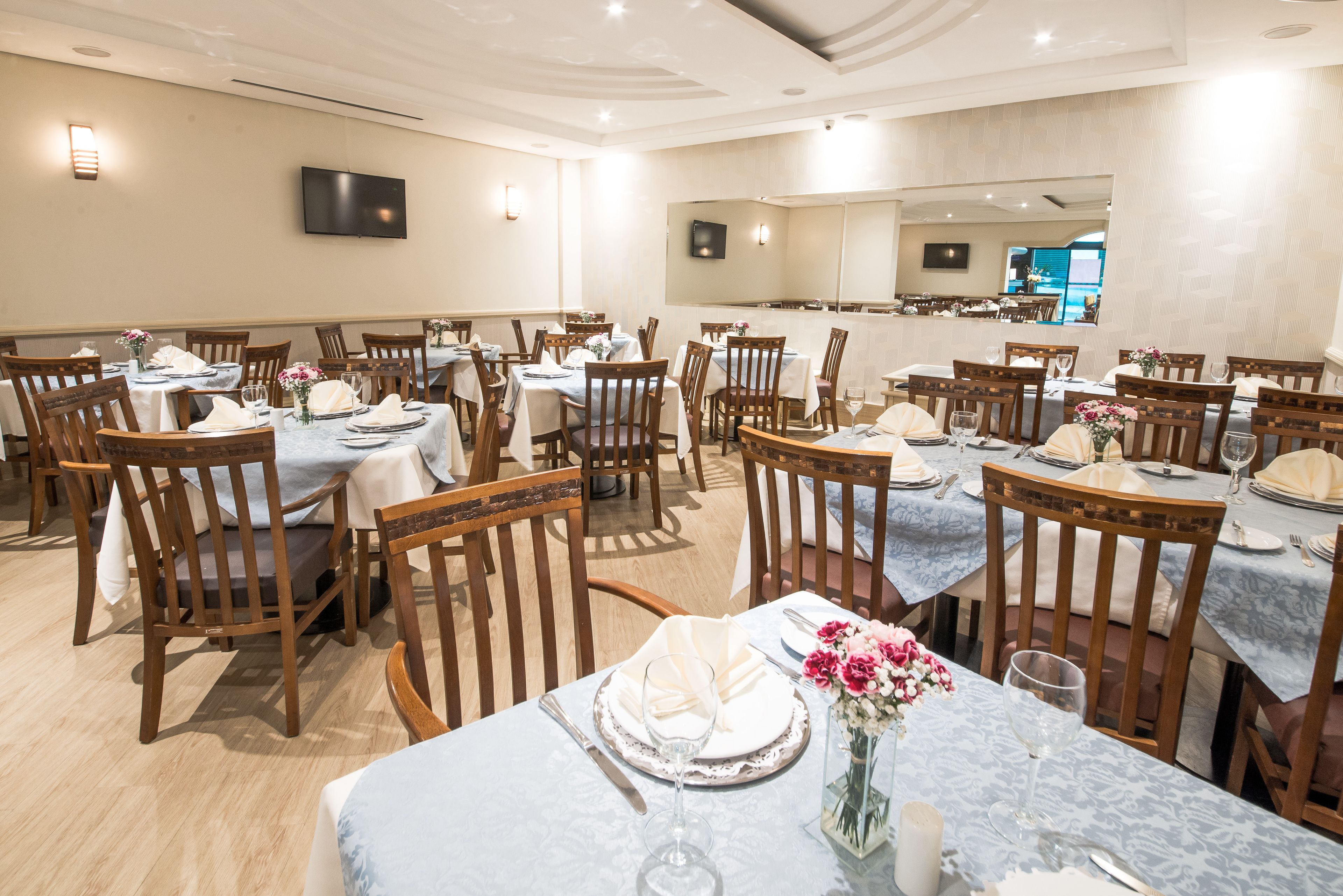 A dining area with multiple tables and chairs, each set with plates, glasses, and cutlery.