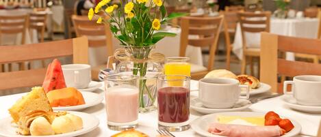 Una escena de desayuno con diferentes platos, bebidas y un florero sobre una mesa.