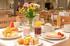 A breakfast setting with various dishes, drinks, and a vase of flowers on a table. - Summit Hotel Monaco (Guarulhos)