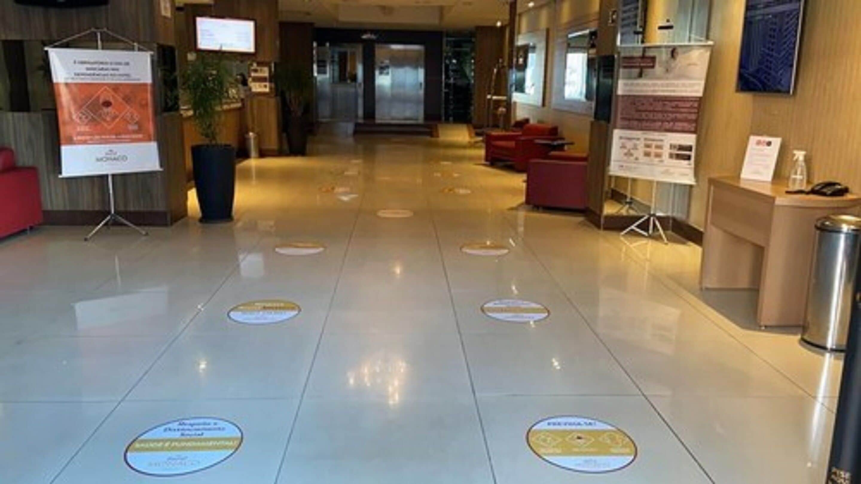 A hotel lobby with a polished floor, reception desk, and informational posters.