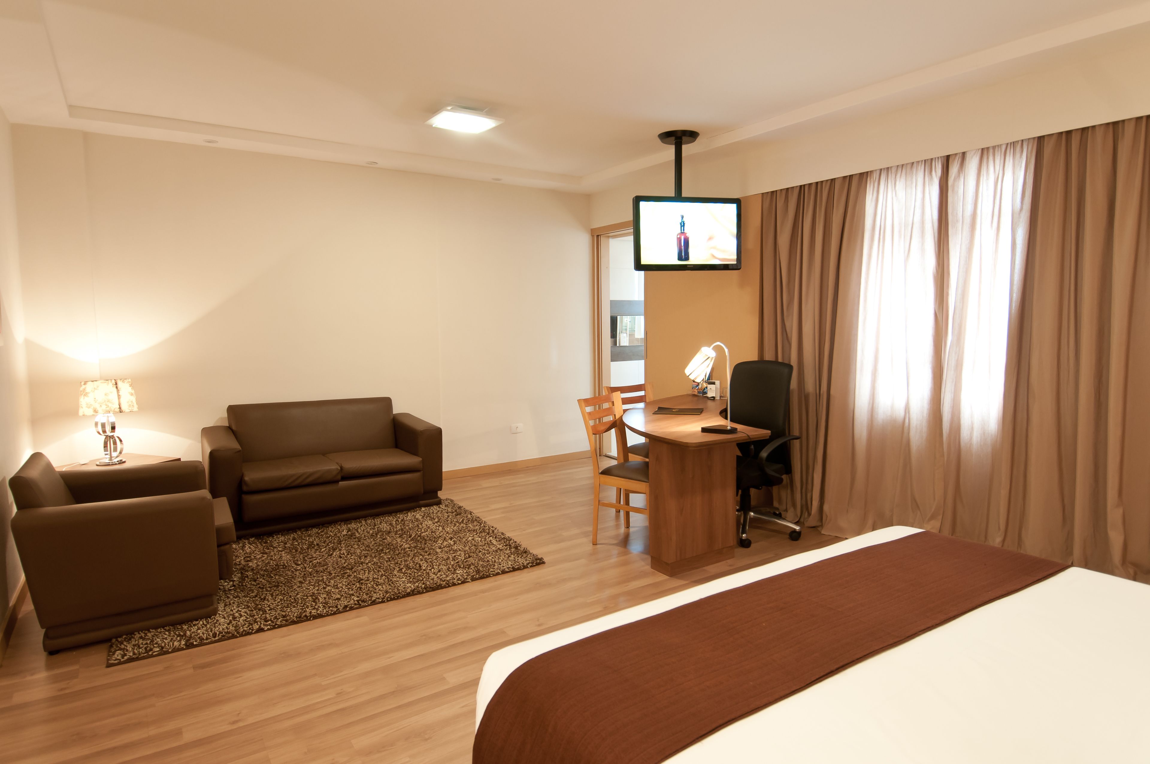 A hotel room with a bed, a desk with a chair, a sofa, a TV, and a lamp.