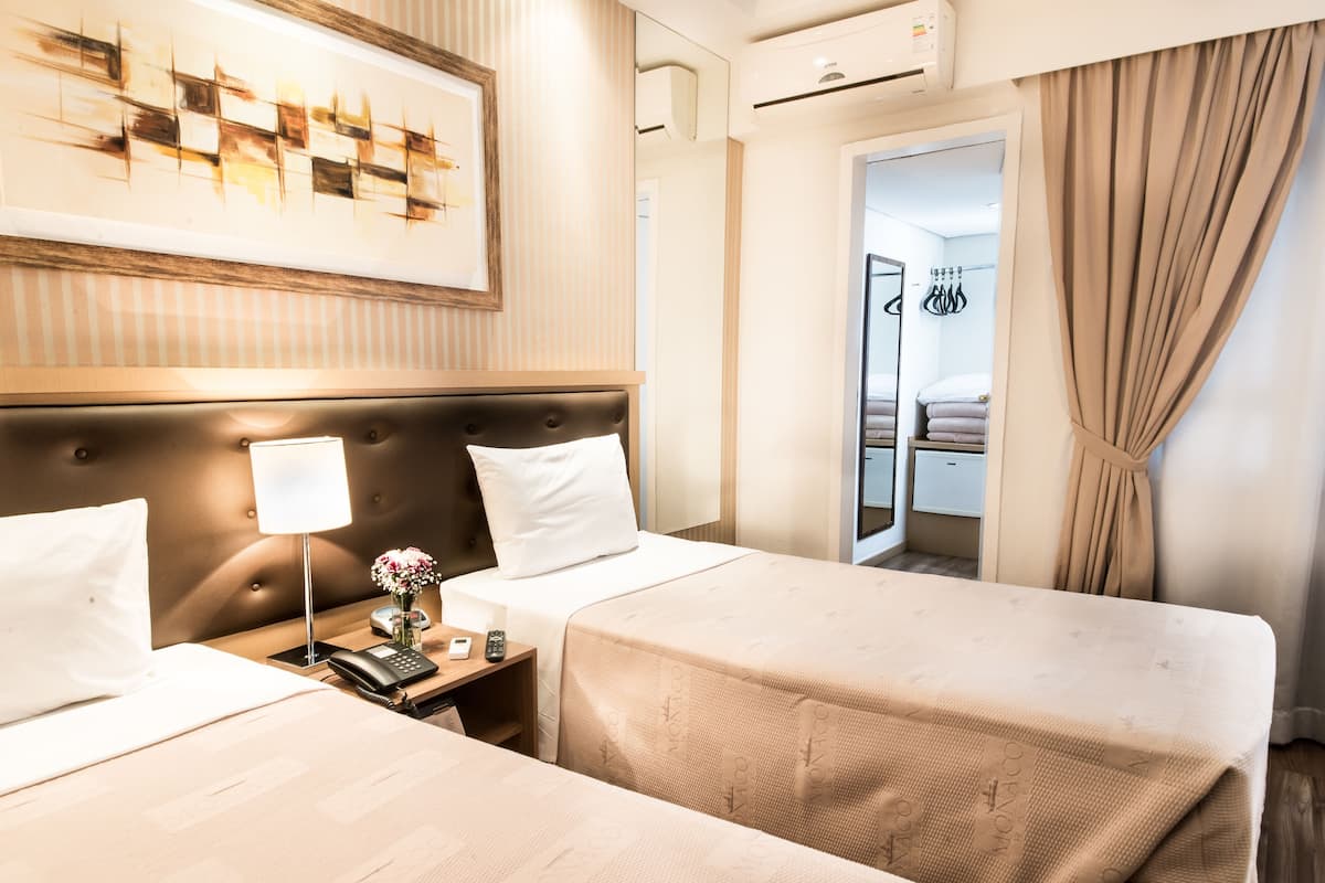 A hotel room with two beds, a headboard, bedside tables, a lamp, a phone, and a painting on the wall.
