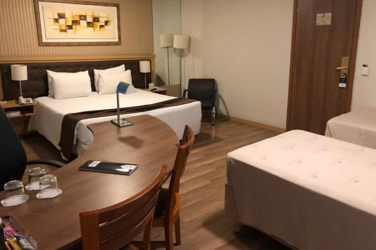 A hotel room with a bed, a desk, a chair, a small table, and a bedside table.