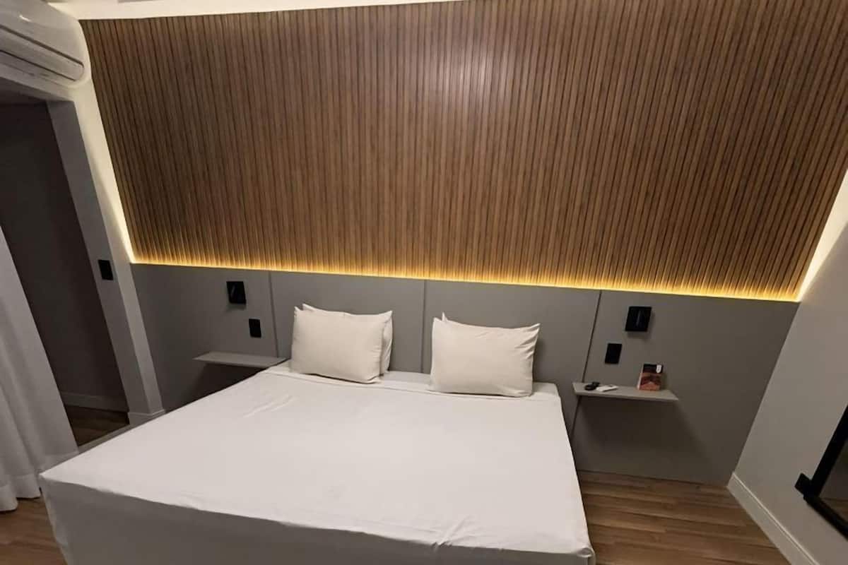 A modern bedroom with a large bed, wooden panel headboard, bedside tables, and a wooden floor.