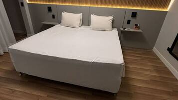 Un dormitorio moderno con una cama grande, cabecera de madera panelada, mesitas de noche y suelo de madera.