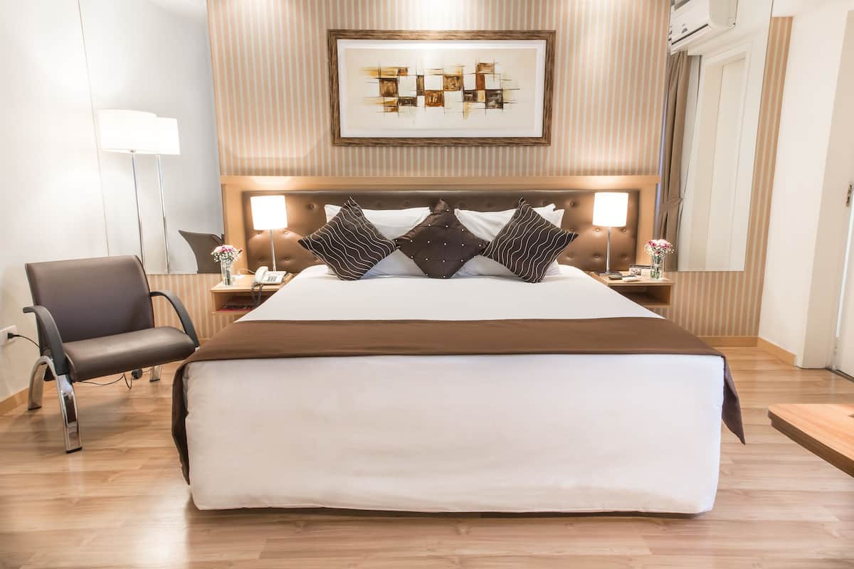 A hotel room with a large bed, a chair, a bedside table with a lamp, and a framed artwork on the wall.