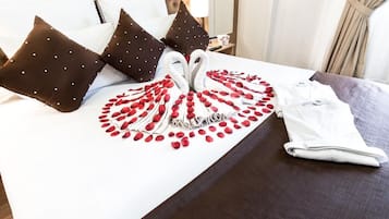 Cama arrumada com um arranjo de pétalas de rosa vermelhas em formato de cisne, almofadas brancas e toalha dobrada.
