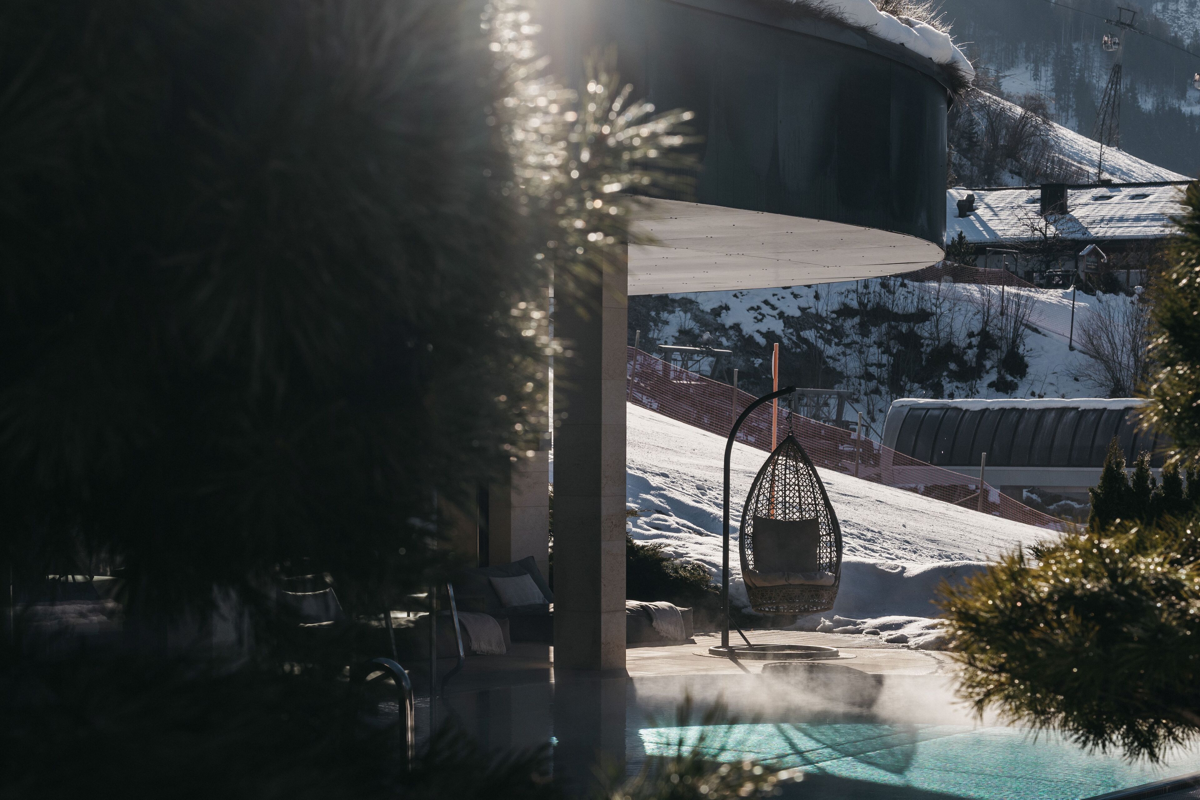 A pool area with a chair and a hanging chair, surrounded by snow-covered hills.