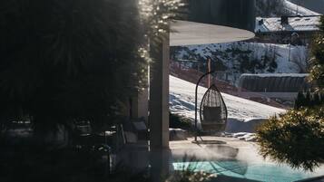 A pool area with a chair and a hanging chair, surrounded by snow-covered hills.