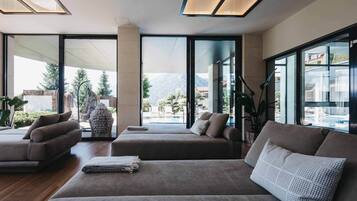 A modern living room with a large sofa set, a coffee table, and a view of a mountainous landscape through large windows.