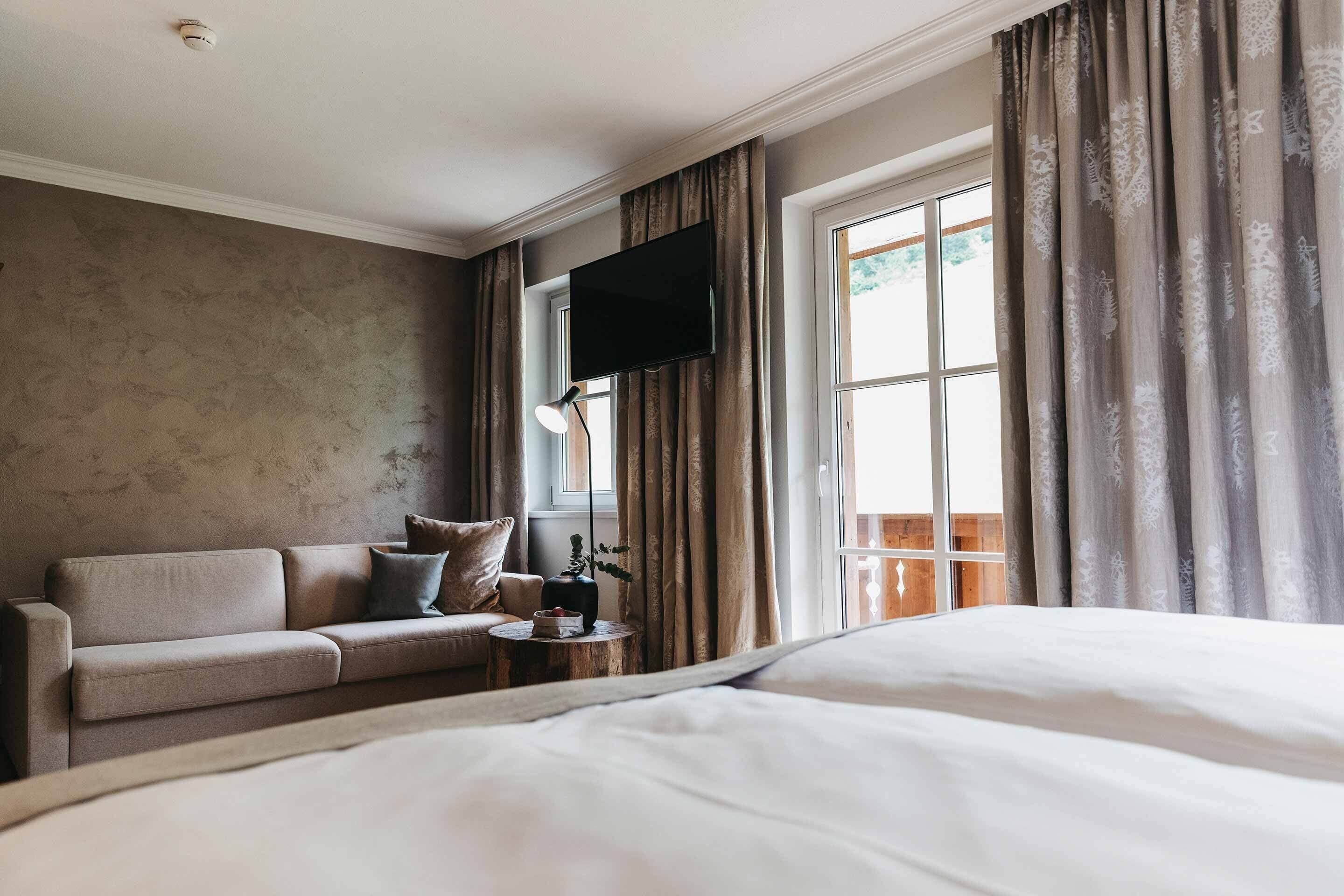 A hotel room with a bed, a sofa, a small table with a plant, and a TV on the wall.