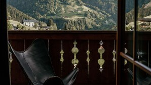 A balcony with a view of mountains, a wooden floor, and a black chair.