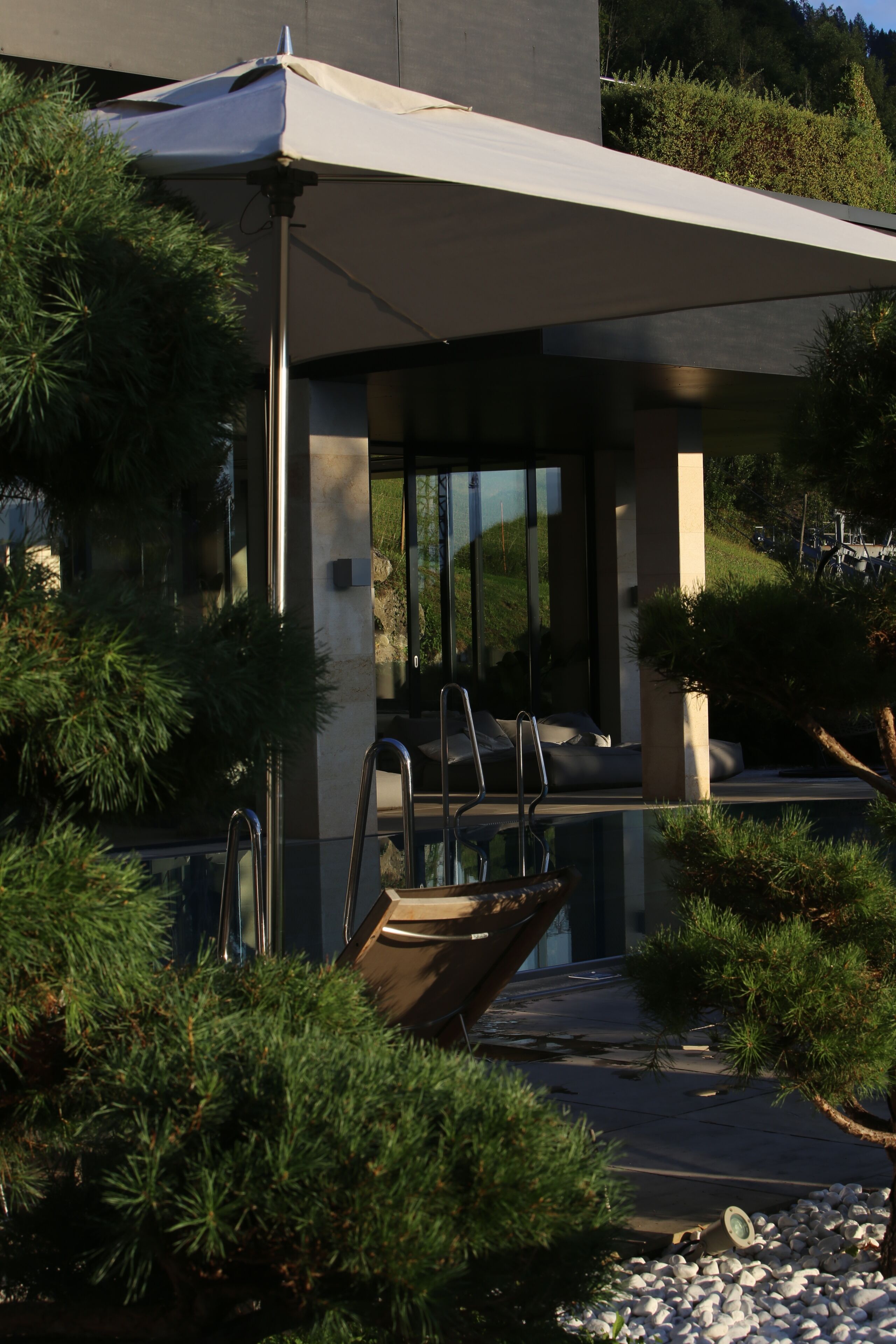 Un edificio moderno con un área de estar al aire libre cubierta, piscina y abundante vegetación.