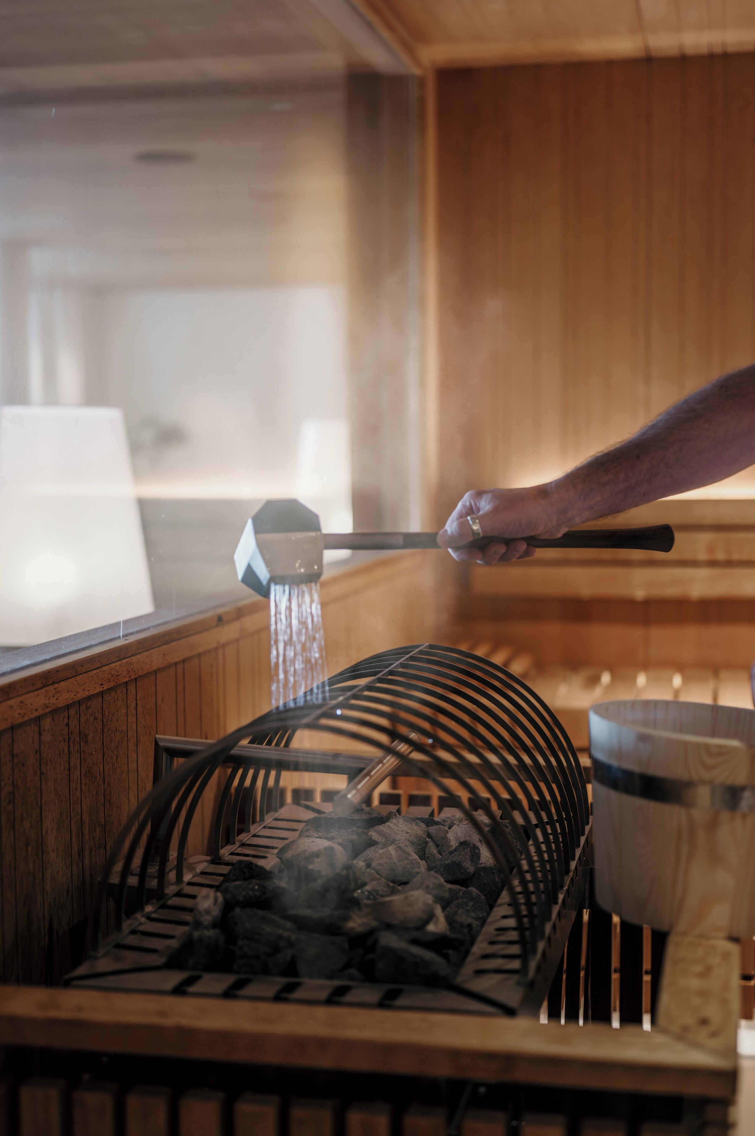 Una sauna con interior de madera, una rejilla metálica para piedras y una mano ajustando un grifo de agua.