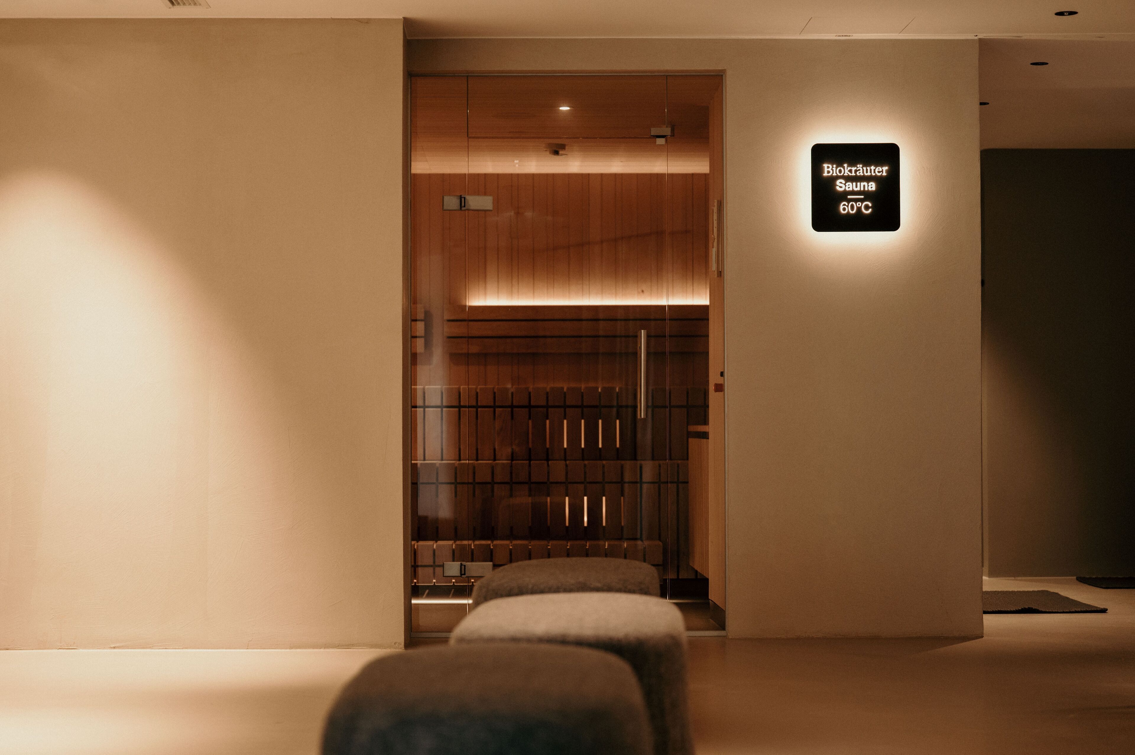 Un espace spa moderne avec un comptoir d’accueil en bois, un panneau indiquant un sauna à 60 °C et un banc au premier plan.