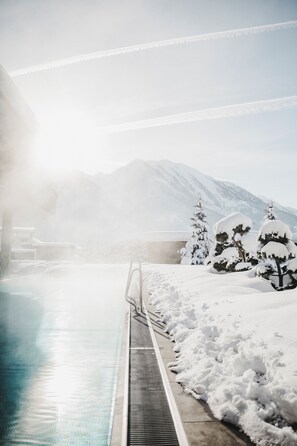 A snow-covered outdoor pool area with a metal railing, surrounded by snow-laden trees and mountains in the background. - Sonnhof Alpendorf - an adults only place (Sankt Johann im Pongau)