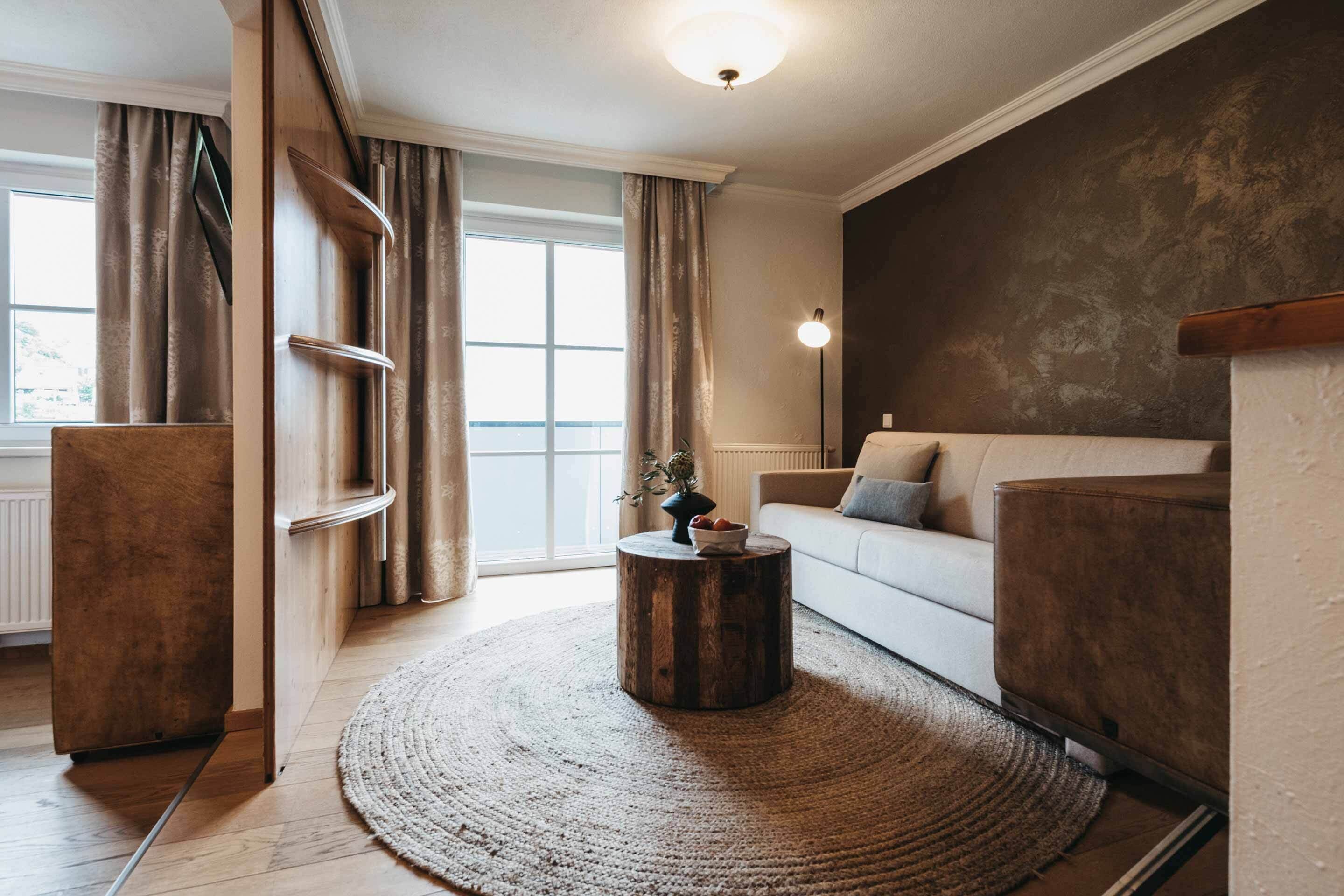 Una sala de estar moderna con una mesa redonda de madera, un sofá blanco y un ventanal con cortinas.