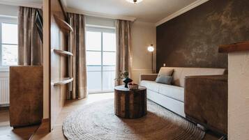 Una sala de estar moderna con una mesa redonda de madera, un sofá blanco y un ventanal con cortinas.