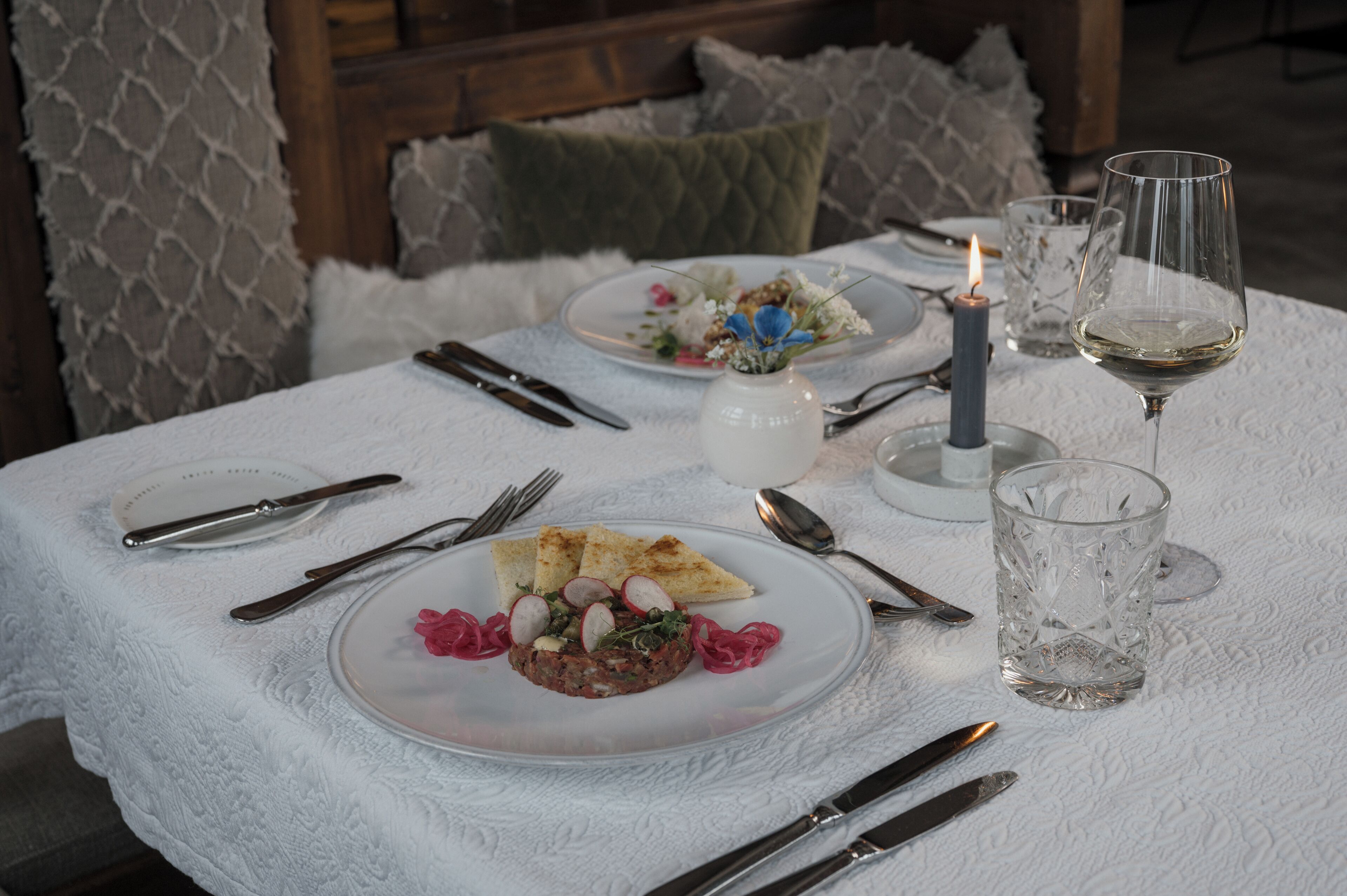 Una mesa servida para una comida, con platos, cubiertos, una vela y vasos.