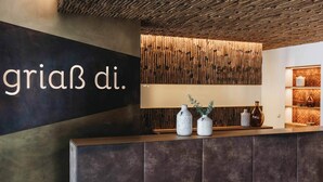 A reception area with a dark wall and a sign that reads "griaβ di." There are two vases on the counter and a wooden wall with vertical slats behind it.