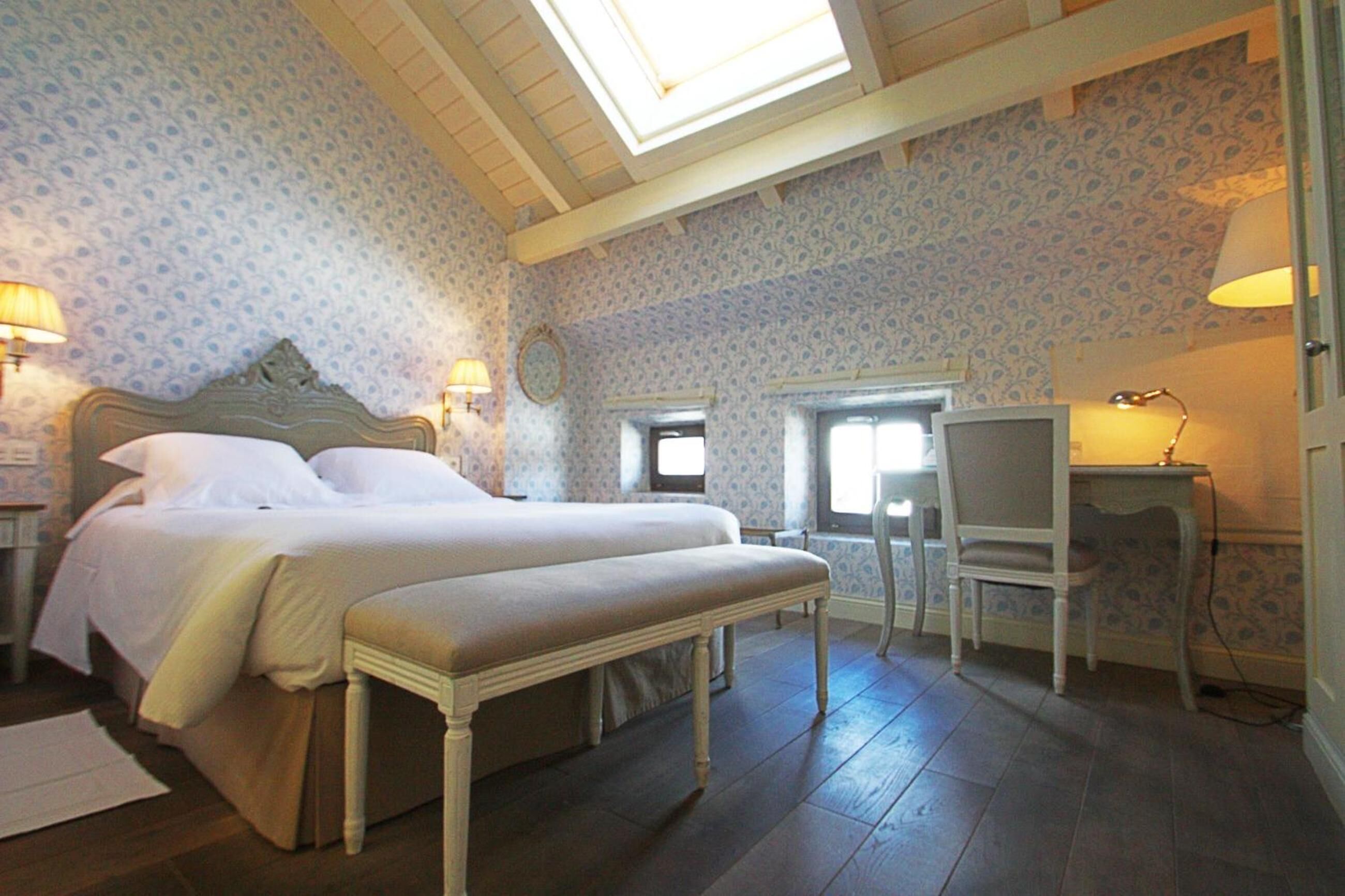 A bedroom with a large bed, a bench, a desk, and two lamps.