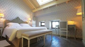 A bedroom with a large bed, a bench, a desk, and two lamps.