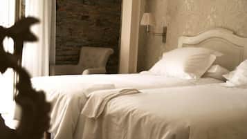A neatly made bed with white linens in a room with a stone wall and a lamp on the wall.