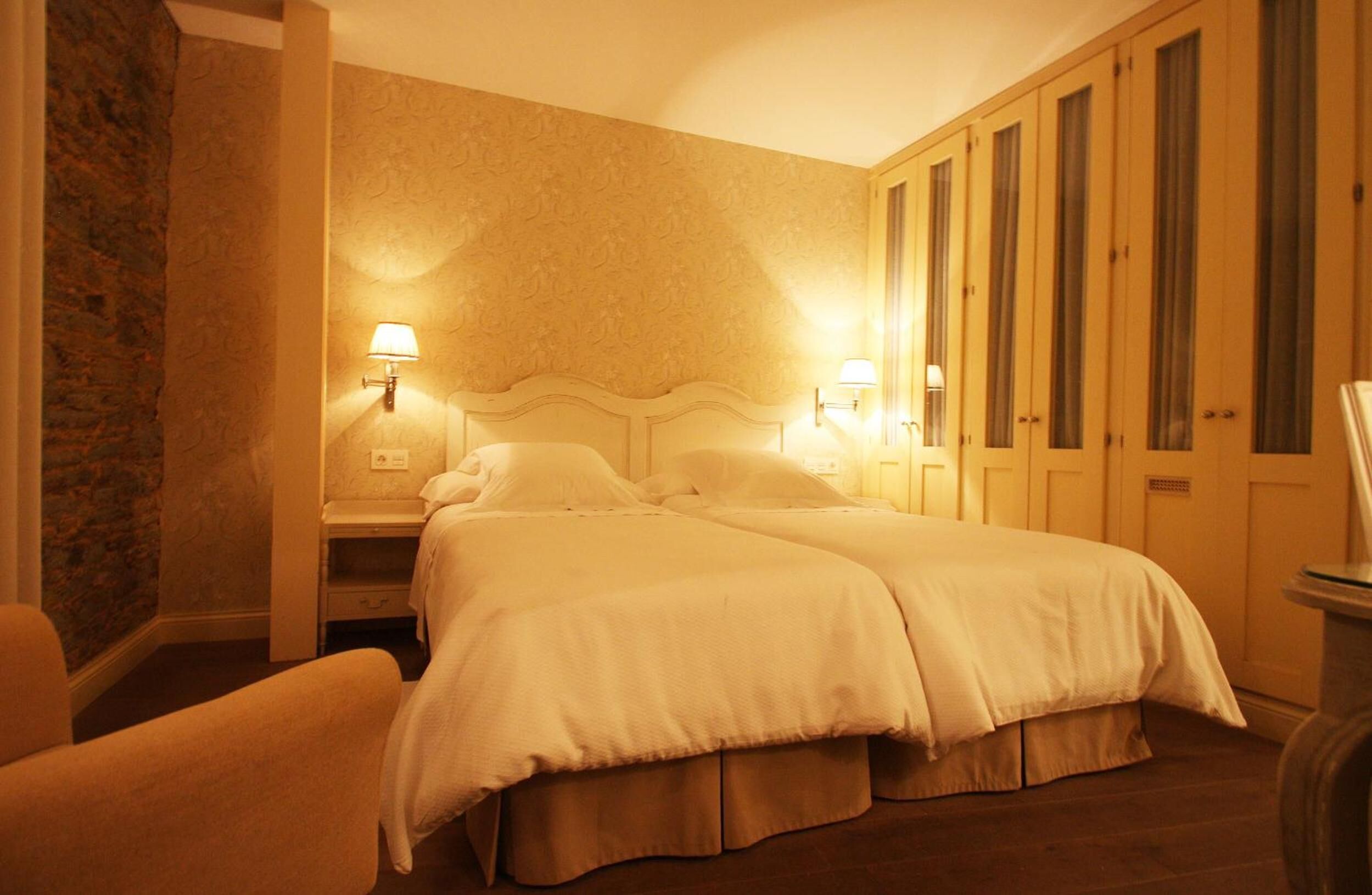 Habitación de hotel con cama doble, dos mesitas de noche con lámparas, un armario y una pared de acento de piedra.