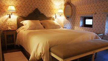 Una cama bien hecha con cabecera, dos lámparas de noche, un ventanal pequeño y un espejo en la pared.