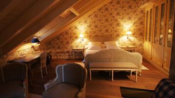 A cozy attic bedroom with a sloped ceiling, a bed with white linens, two bedside lamps, and a wooden desk with a lamp.