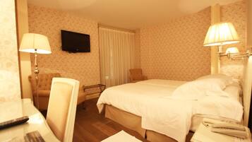 Habitación de hotel con cama, lámparas de noche, televisor montado en la pared, una silla y escritorio con control remoto.