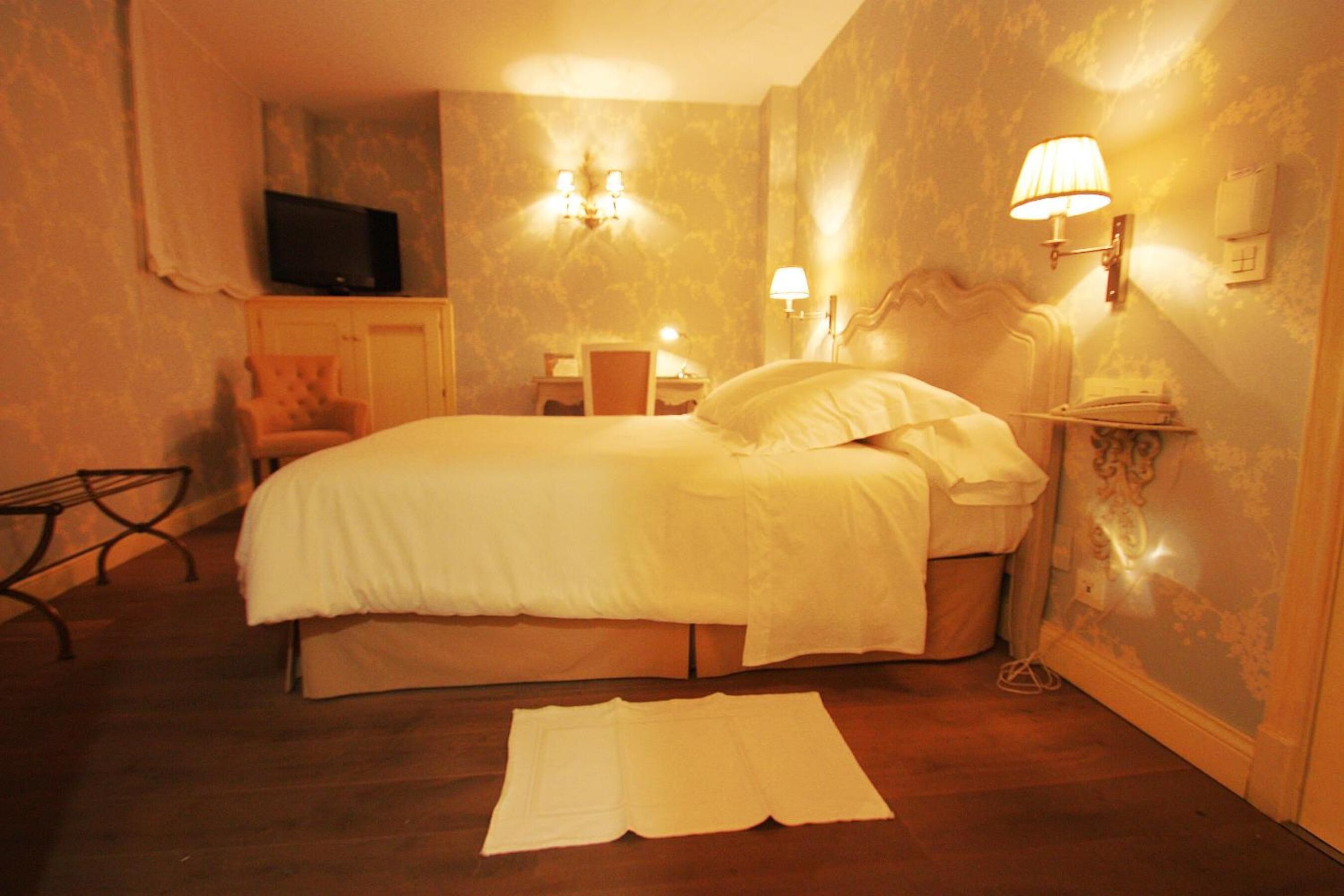Ein Hotelzimmer mit einem Bett, einem Fernseher, einem Sessel und einem Schreibtisch mit Lampe.