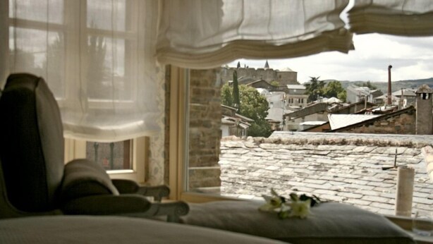 Una habitación con vistas a un pueblo histórico, una cama y una ventana con cortinas translúcidas.