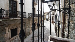 Una estrecha calle adoquinada con edificios de piedra, barandillas de hierro forjado negro y una chimenea de piedra.