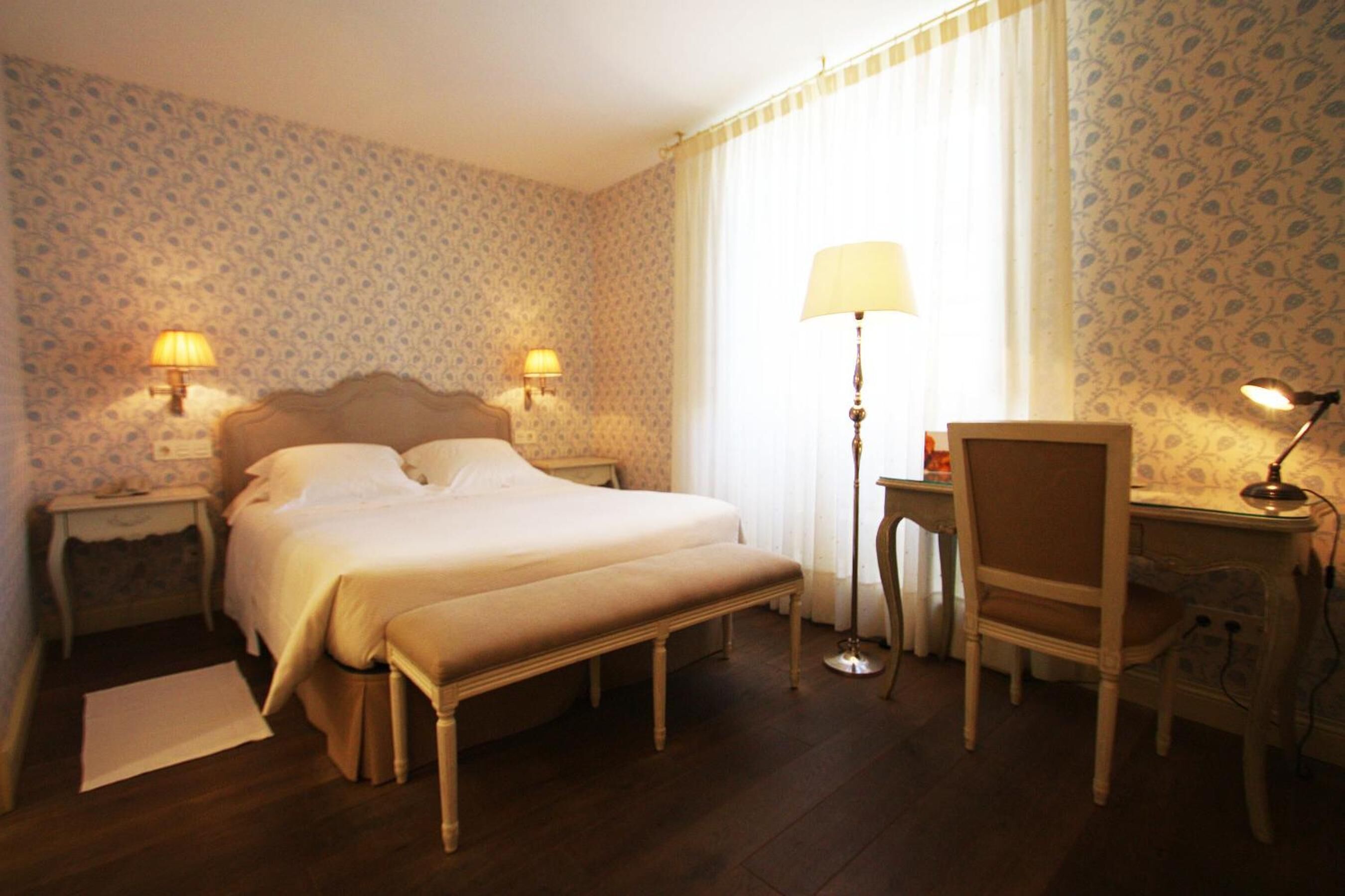 A hotel room with a large bed, two bedside lamps, a desk with a chair, and a floor lamp.
