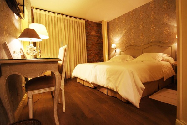 A hotel room with a bed, a desk with a lamp, a chair, and a curtain.